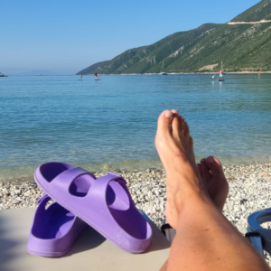 sunbathing legs and purple sandals by the sea