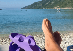 sunbathing legs and purple sandals by the sea